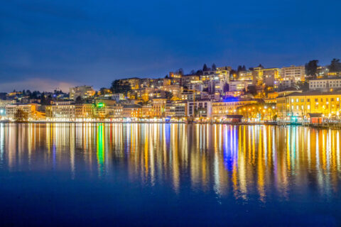 Night panorama oа уmbankment of lake Lugano and town Lugano in blue hour and reflections in water of street lights